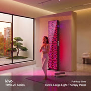 A woman stands on a yoga mat in a modern wellness room beside a wall-mounted extra large KIVO red LED light therapy panel