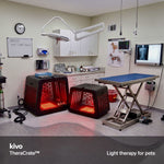 Two Kivo red light therapy pet crates glowing with red light inside a veterinary exam room, with a surgical table, medical cabinets, and whiteboards in the background. A text overlay at the bottom reads 'The TheraCrate Red light therapy for Dogs, Cats, and other Furry Friends.